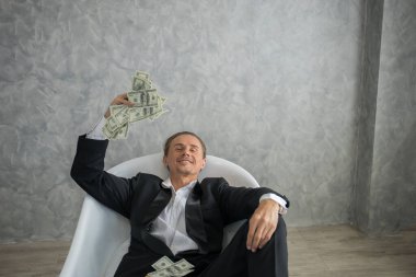 Dolar banknotlarıyla dolu küvette yatan zengin bir işadamı. Başarı iş konsepti.