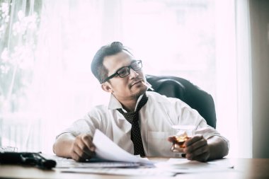 Gangster, elinde viski bardağı ve sigarayla oturmuş kara iş haritasını inceliyor.