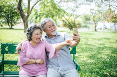 Yaşlı çift parkta akıllı telefonlarıyla selfie çekiyor.