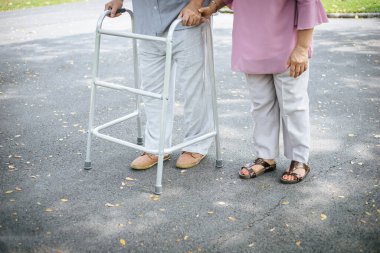 Destek için yürüteç kullanan kıdemli hastasına yardım ediyor.