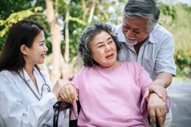 Hemşire tekerlekli sandalyedeki yaşlı hastaya bakıyor. Doktor yaşlı engellilerle konuşuyor. 