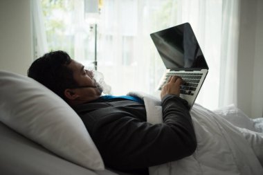 Ofiste oksijen maskesiyle çalışan takım elbiseli bir iş adamı. Hasta adam ofiste yalnız çalışıyor.