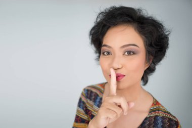 Genç kız beyaz arka planda sessiz jest yapıyor.