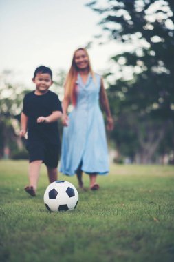 Küçük çocuk parkta annesiyle futbol oynuyor.