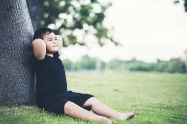 Küçük çocuk ağacın altında oturmuş bir şeyler düşünüyor.