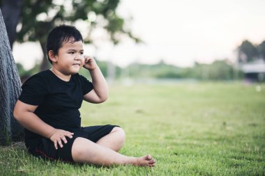 Küçük çocuk ağacın altında oturmuş bir şeyler düşünüyor.
