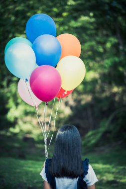Genç kız elinde renkli balonlar tutuyor.