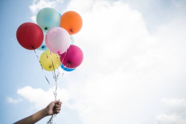 Genç kız elinde renkli balonlar tutuyor.