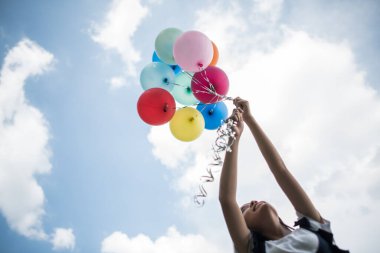 Genç kız elinde renkli balonlar tutuyor.