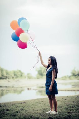 Genç bir kadın elinde renkli balonlar tutuyor.