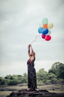 Genç bir kadın elinde renkli balonlar tutuyor.