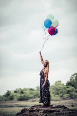 Genç bir kadın elinde renkli balonlar tutuyor.