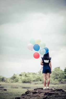 Genç bir kadın elinde renkli balonlar tutuyor.