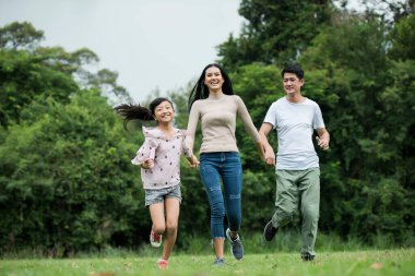 Mutlu aile eğleniyor. Anne, baba ve kız parkta koşuyorlar..