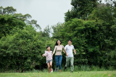 Mutlu aile eğleniyor. Anne, baba ve kız parkta koşuyorlar..