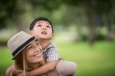 Mutlu genç anne ve oğul sırtına binen küçük çocuğa gülüyorlar. Aile kavramı.