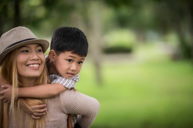 Mutlu genç anne ve oğul sırtına binen küçük çocuğa gülüyorlar. Aile kavramı.
