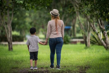Anne ve oğlunun ev bahçesinde el ele tutuşup yürüdüğü arka manzara. Aile kavramı.