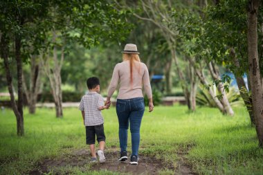 Anne ve oğlunun ev bahçesinde el ele tutuşup yürüdüğü arka manzara. Aile kavramı.