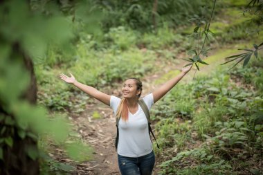 Sırt çantalı genç bir kadın ormanda yürürken kollarını kaldırdı..