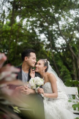 Gelin ve damat, arka planda yeşil park olan bir şubede oturuyorlar..