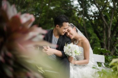 Gelin ve damat, arka planda yeşil park olan bir şubede oturuyorlar..