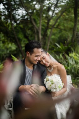 Gelin ve damat, arka planda yeşil park olan bir şubede oturuyorlar..