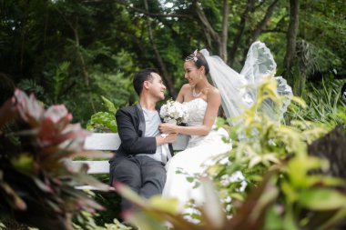 Gelin ve damat, arka planda yeşil park olan bir şubede oturuyorlar..