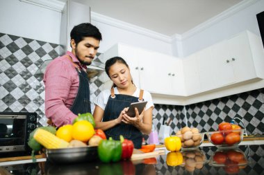Mutlu genç çift, evde yemek pişirirken dijital tablet kullanarak yemek yapma yöntemini kullanıyor..