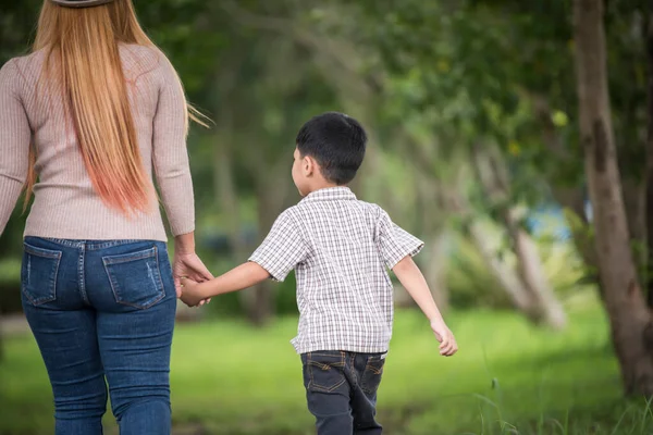 Anne ve oğlunun ev bahçesinde el ele tutuşup yürüdüğü arka manzara. Aile kavramı.