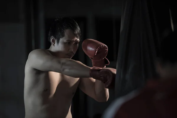 ジムでパンチングバッグの上でボクシングを練習している若いアジア人男性の肖像画 — ストック写真