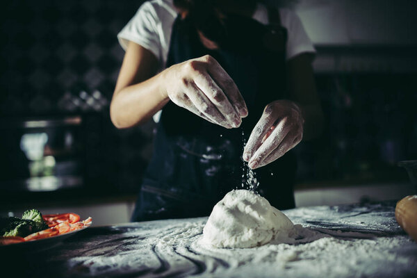 Woman pouring flour on dough while kneads preparing for make pizza. Cooking concept.