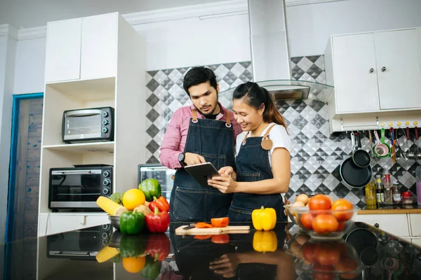 Mutlu genç çift, evde yemek pişirirken dijital tablet kullanarak yemek yapma yöntemini kullanıyor..
