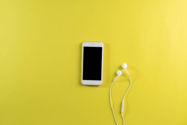 Üst görünüm cep telefonu ve kulaklık beyaz masada.