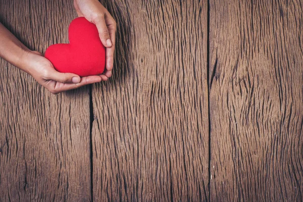 Hand holding red heart on wood background