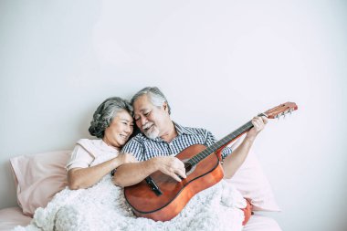 Yaşlı çift yatak odasında akustik gitar çalarak rahatlar.