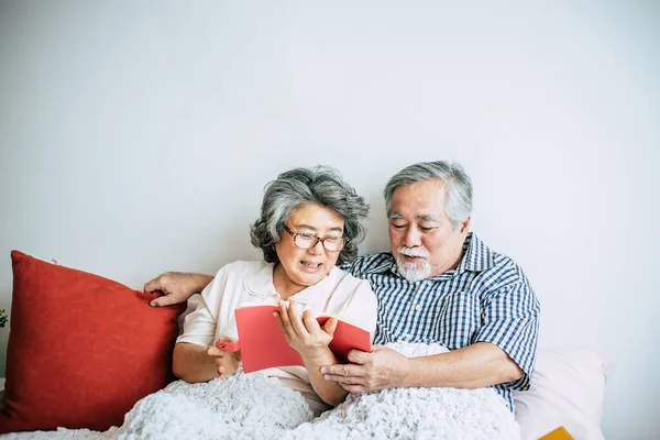 高齢者のカップルベッドの上に横たわると本を読んで — ストック写真