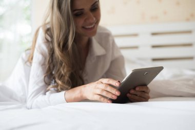 Mutlu kadın tablet bilgisayarla yatakta yatıyor. 