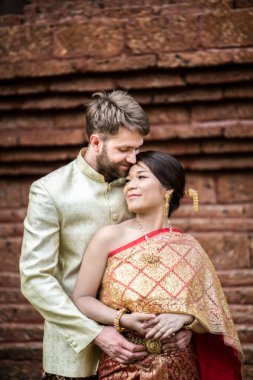 Asyalı gelin ve beyaz damat Tayland elbisesiyle romantik vakit geçiriyorlar.