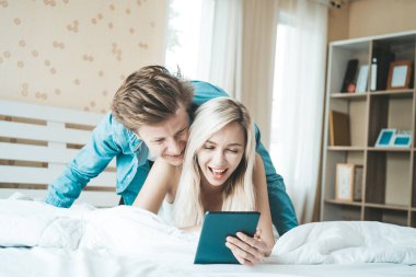 Mutlu çift yatakta tablet bilgisayar kullanıyor.