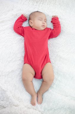 Kırmızı tişörtlü bebekler yatakta uyur.