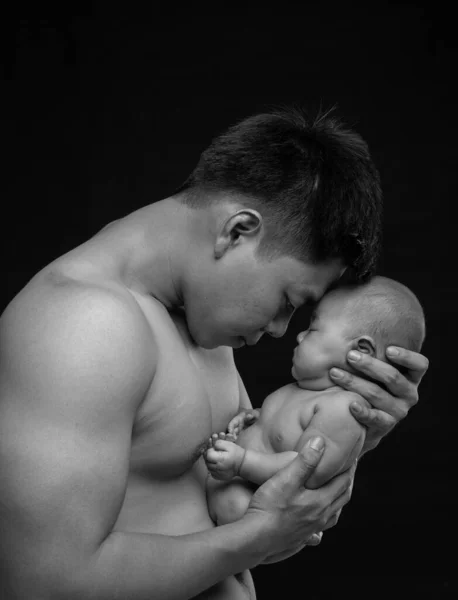 The baby sleeps in the hands of a strong father.