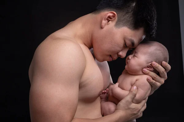 The baby sleeps in the hands of a strong father.