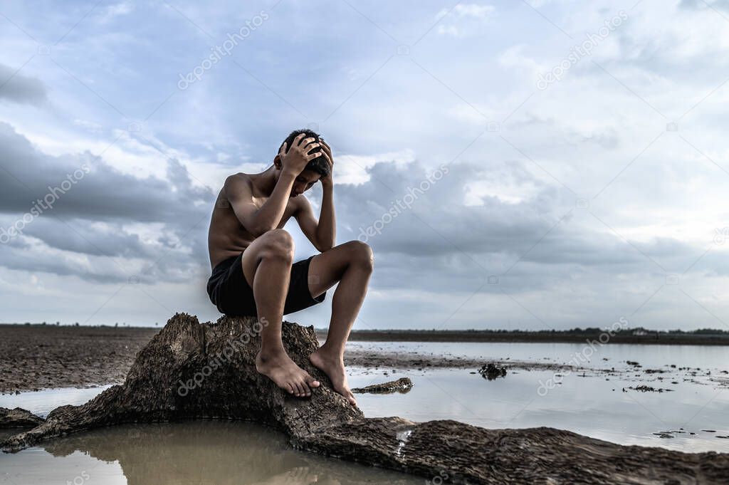 A man sat bent his knees and put his hands on his head, on the base of the tree and surrounded by water.