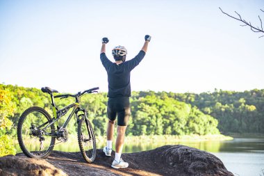 Dağ bisikletçileri bir bisikletle dağın tepesinde dururlar ve ellerini iki tarafa kaldırırlar..