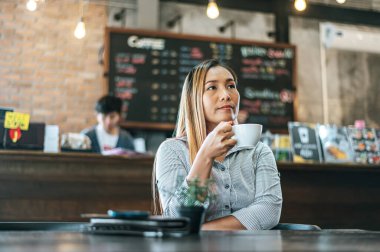 Kadın kafeteryada mutlu bir şekilde oturup kahve içiyor.