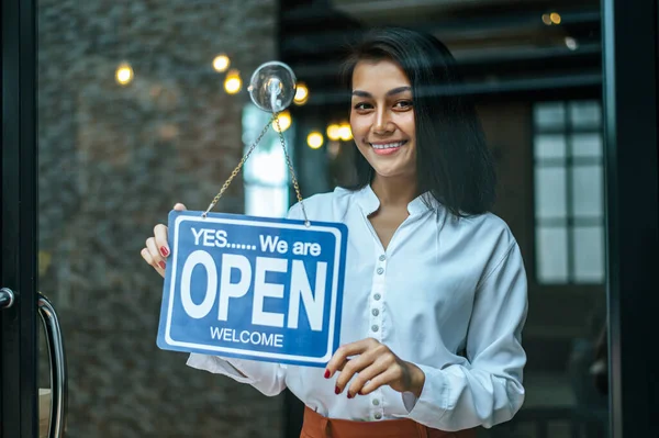 Kadın dikilir ve dükkanın penceresinden geniş bir tabela açar ve gülümser..