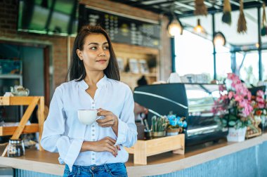 Kafede elinde bir fincan kahveyle duran bir kadın.