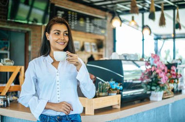 Kafede elinde bir fincan kahveyle duran bir kadın.