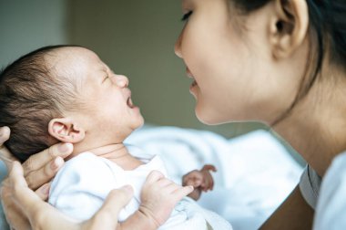 Yeni doğan bebek beyaz giyiyordu ve annesinin kollarında ağlıyordu..